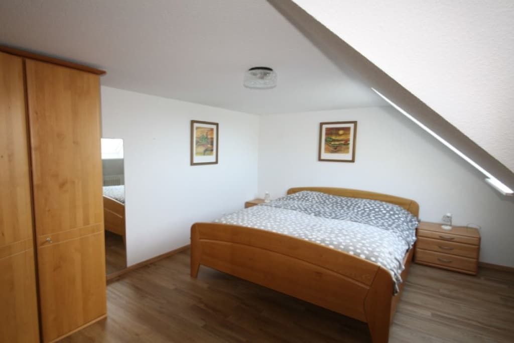 Quarto com cama de madeira, mesa de cabeceira, guarda-roupa e duas imagens emolduradas na parede.