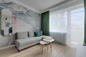 A modern living room with a sofa, a round coffee table, and a large window with curtains. - Apartament Tamara by Q4 Apartments  (Gdańsk)