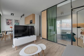 A modern living room with a flat-screen TV, a dining area with chairs, and a glass partition. - Apartament Tamara by Q4 Apartments  (Gdańsk)