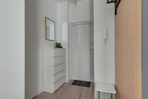 A hallway with a white wall, a door, a small white table, and a plant on a cabinet. - Apartament Tamara by Q4 Apartments  (Gdańsk)