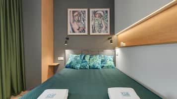 Quarto de hotel com cama, cortinas verdes, cabeceira, duas imagens emolduradas e mesa de cabeceira.
