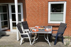 Eine Terrasse im Freien mit Tisch und Stühlen, einer Ziegelwand und einem Fenster.