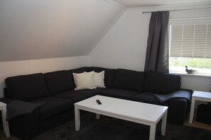 Un moderno salón con un sofá seccional negro, una mesa de centro blanca y una ventana con persianas.