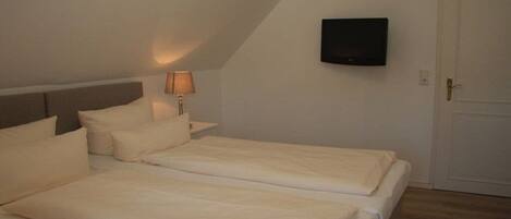 A room with two beds, a bedside table with a lamp, a television on the wall, and a door.