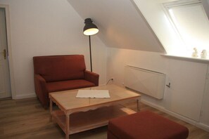 Ein kleiner, gemütlicher Raum mit einem roten Sofa, einem Holztisch und einer Stehlampe.