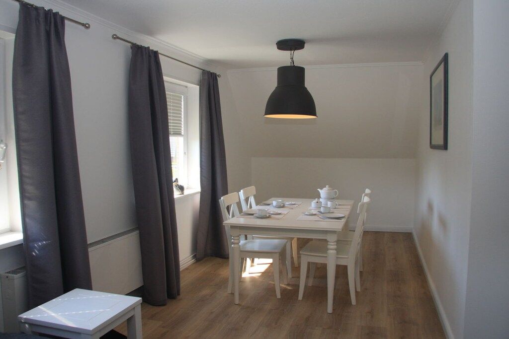 A dining area with a table set for four, a hanging pendant light, and a window with curtains.
