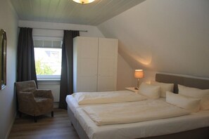 Un dormitorio con cama, una silla, un armario y una ventana con cortinas.