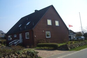 Ein rotes Backsteinhaus mit einem steilen Satteldach, einer Veranda und einer Fahnenstange mit einer Flagge.