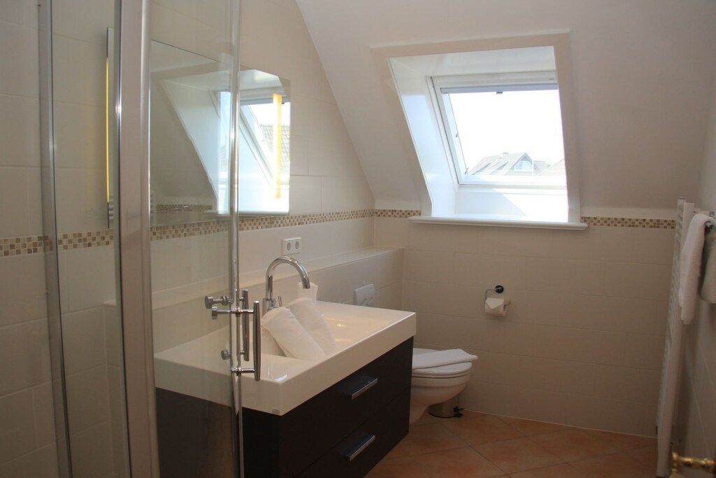 Ein Badezimmer mit Duschkabine aus Glas, einem weißen Waschbecken mit Spiegel, einem Fenster über der Toilette und einem Handtuchhalter.