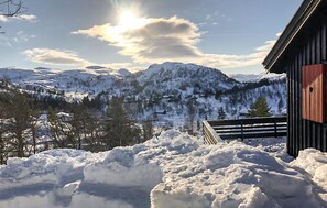 Et sneklædt bjerglandskab med en hytte og et træstakværk i forgrunden.