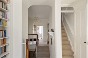 A hallway with a bookshelf, a staircase, and a door leading to another room. - Grade II Listed House & Garden in Idyllic Village (Poughill)
