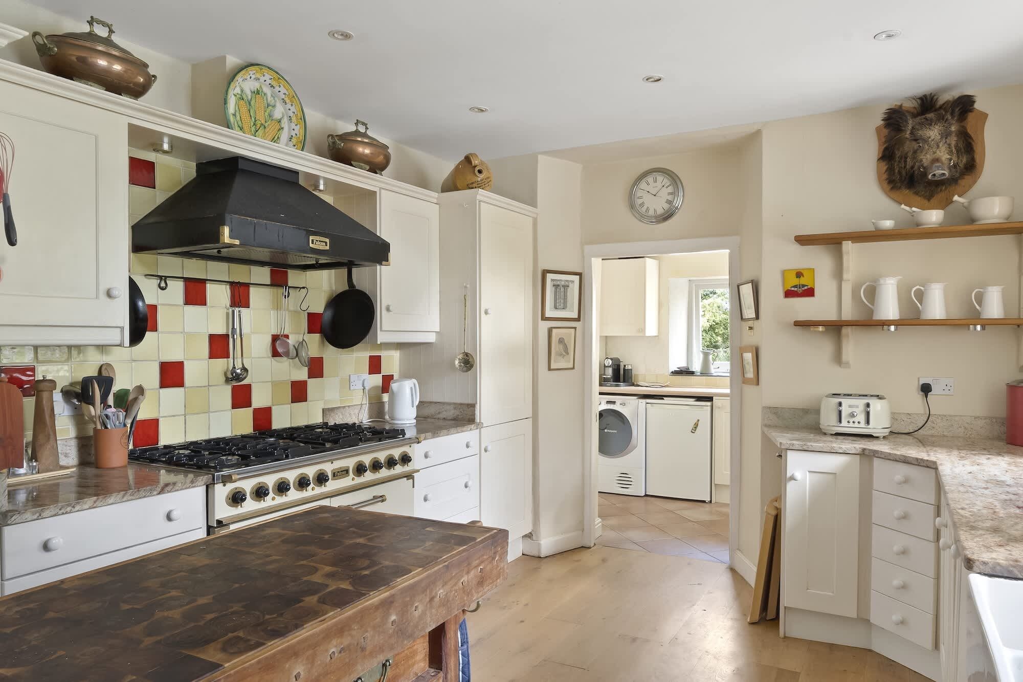 A kitchen with a stove, oven, and various kitchen utensils. There is a washing machine and a toaster in the adjacent room.