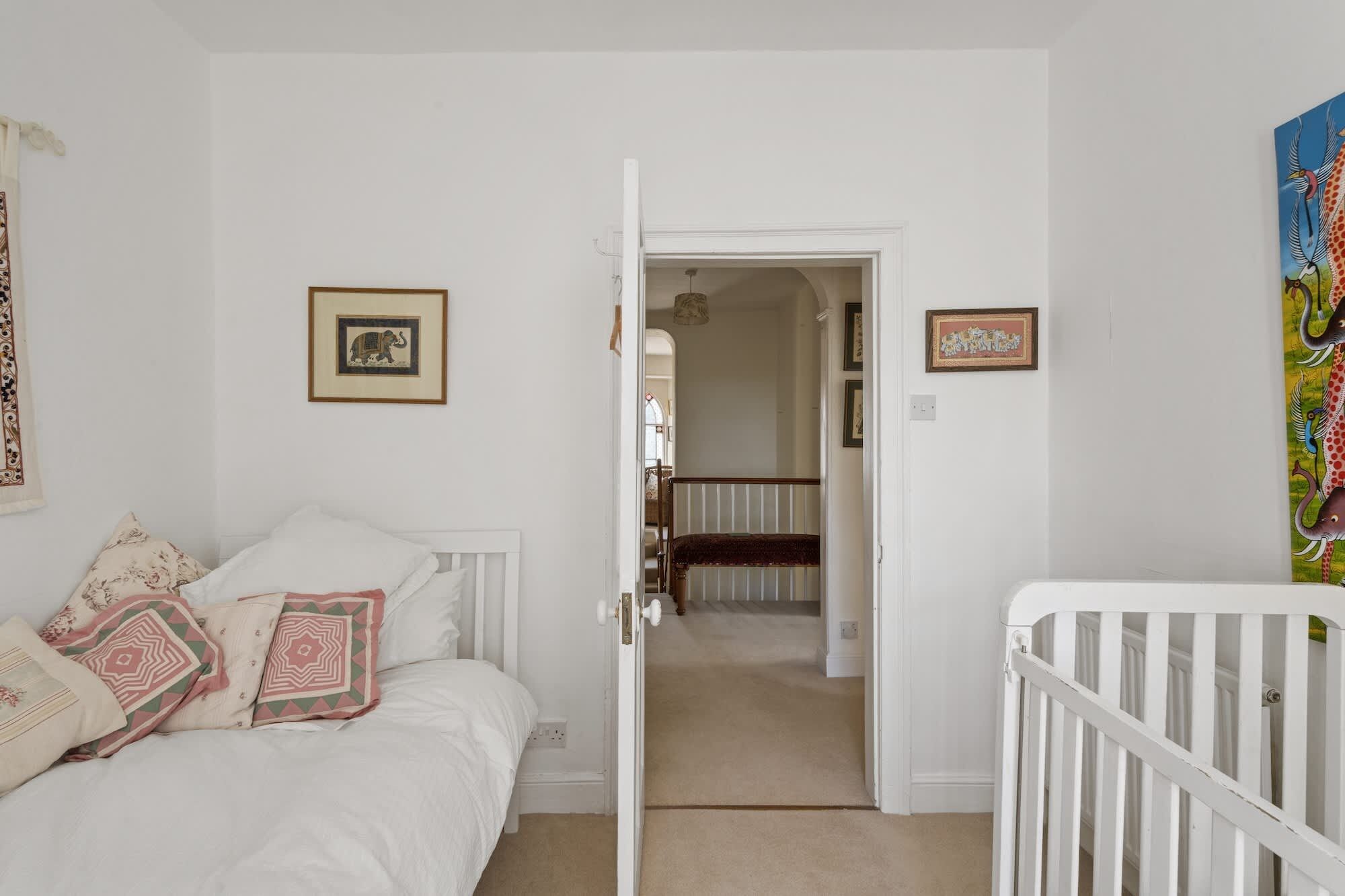 A bedroom with a bed, a crib, and a hallway leading to a staircase.
