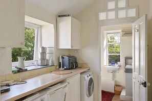A compact kitchen with a washing machine, a coffee maker, and a sink. - Grade II Listed House & Garden in Idyllic Village (Poughill)