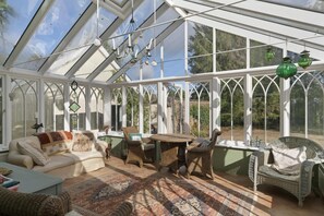 A conservatory with a glass ceiling, wicker furniture, and a patterned rug. - Grade II Listed House & Garden in Idyllic Village (Poughill)