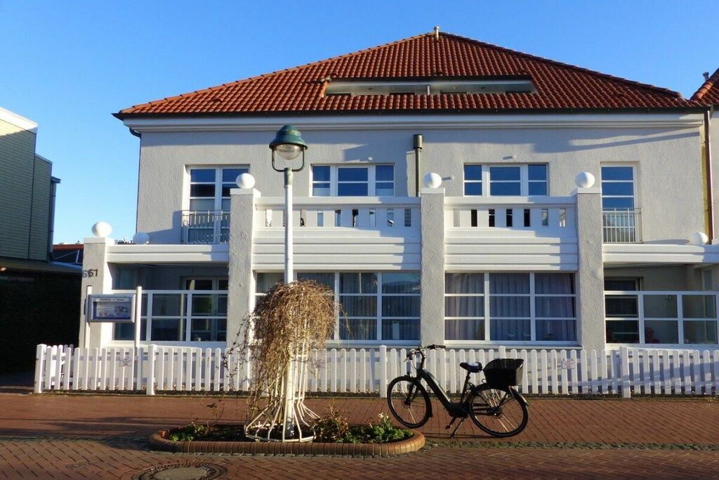 Un bâtiment à la façade blanche, doté d’un toit recouvert de tuiles rouges et d’une clôture en bois peinte en blanc.
