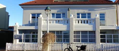 Un bâtiment à la façade blanche, doté d’un toit recouvert de tuiles rouges et d’une clôture en bois peinte en blanc.
