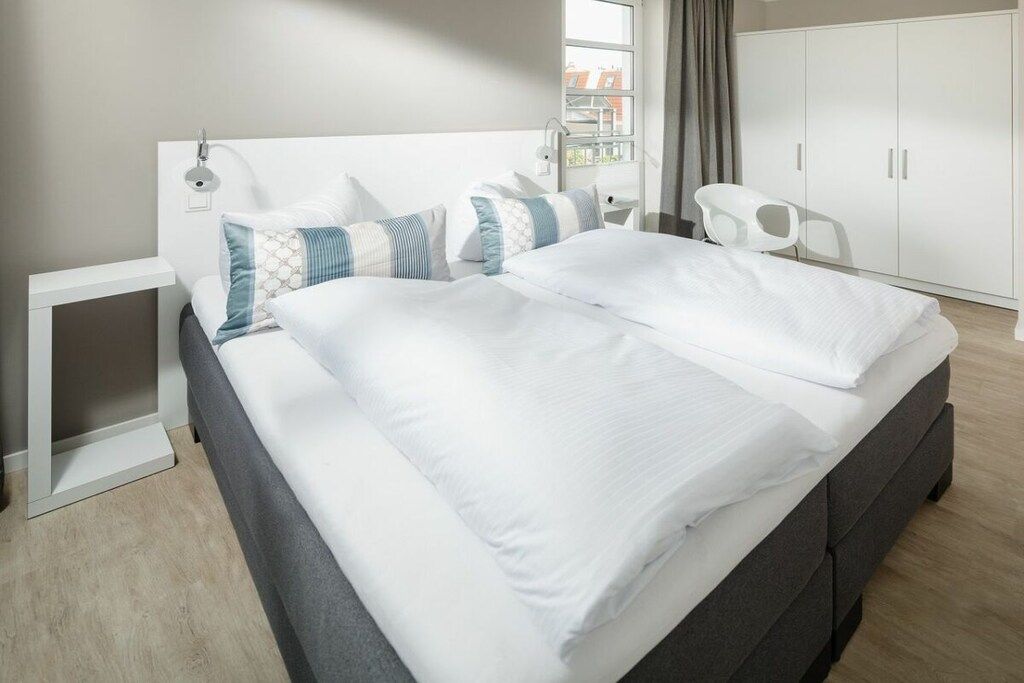 Habitación de hotel moderna con una cama grande, mesitas de noche, un armario y vistas a la ciudad.