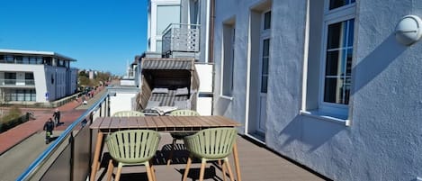 A balcony with a wooden table and chairs, a railing, and a building with windows and a balcony.
