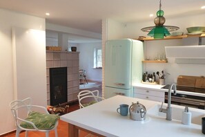 A modern kitchen with a white island, a green hanging light fixture, and a white refrigerator. - Holiday home Seehöft (Hohwacht)