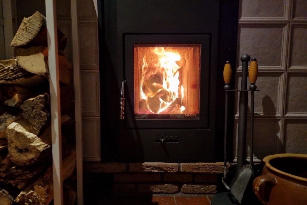 A wood-burning stove with logs, a chimney, and a pot on the right side.