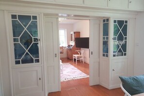 Ein Zimmer mit weißen Türen, Holzboden, einem weißen Stuhl und einem Bett mit blauem Kissen.