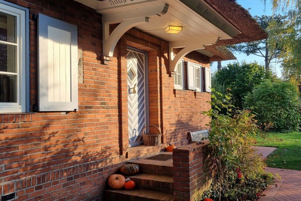 A brick house with a white door, a porch with steps, and a basket on the step.
