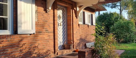 A brick house with a white door, a porch with steps, and a basket on the step.