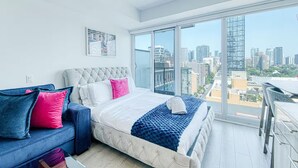 Un dormitorio moderno con una cama grande, un sofá y vista a la ciudad a través de un ventanal de pared a techo.
