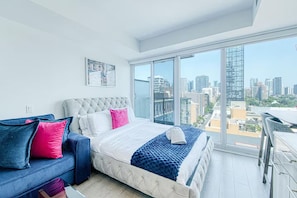 A modern bedroom with a large bed, a sofa, and a city view through a floor-to-ceiling window. - StayToronto - Bright Studio Retreat with Sofa Bed - Prime Location (Toronto)