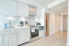 A modern kitchen with white cabinetry, a stainless steel refrigerator, an oven, and a microwave. - StayToronto - Bright Studio Retreat with Sofa Bed - Prime Location (Toronto)