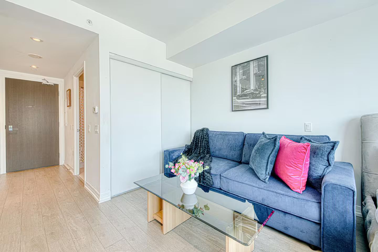 A modern living room with a glass coffee table, a blue sofa with cushions, and a grey armchair.