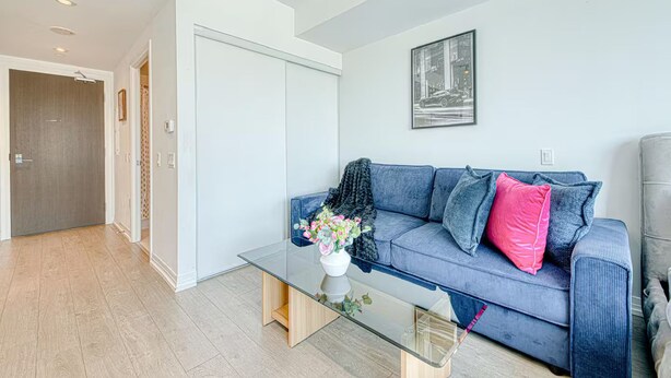 Una sala de estar moderna con una mesa de centro de vidrio, un sofá azul con cojines y un sillón gris.