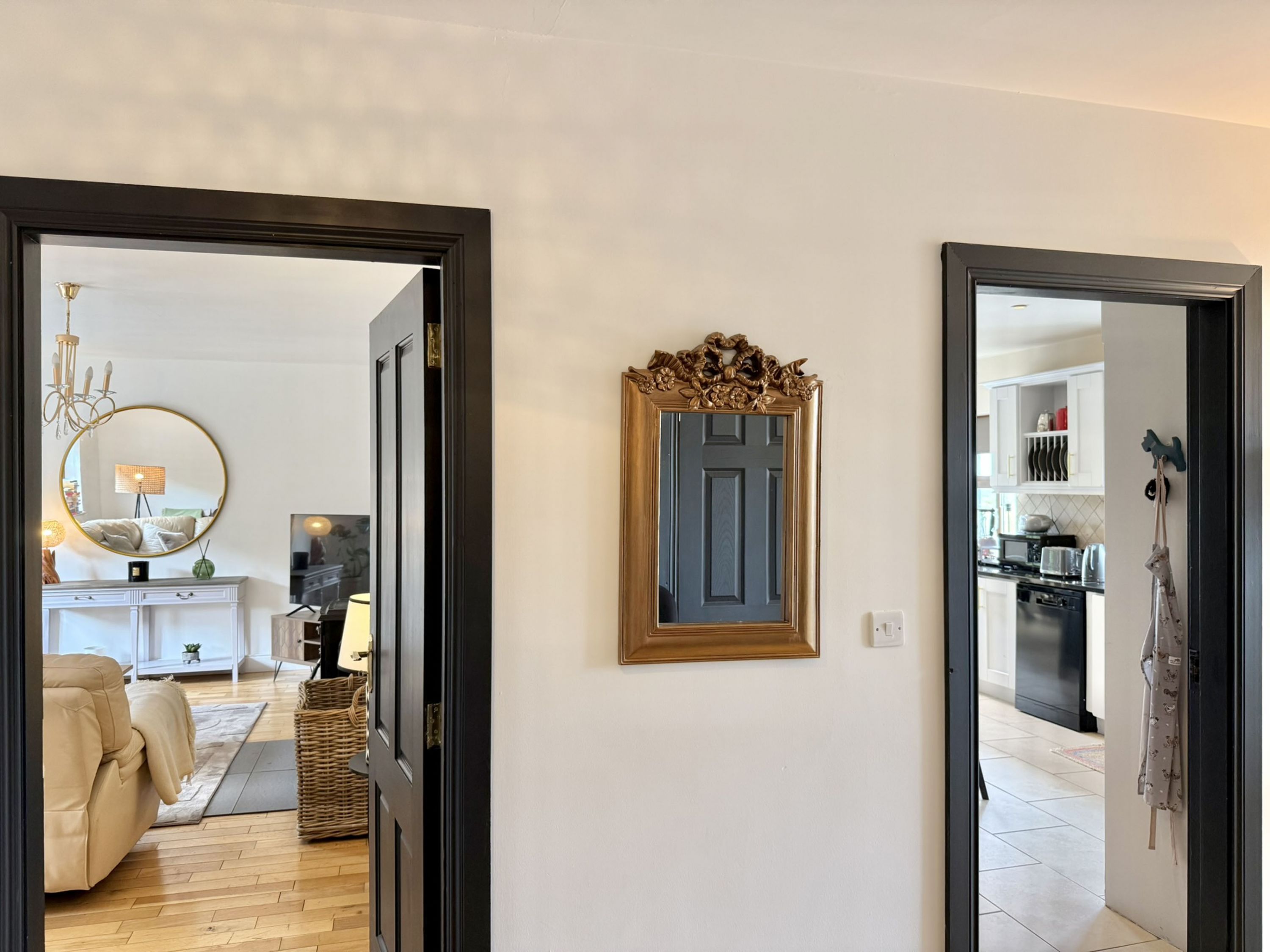 Un pasillo con un espejo, una puerta y vista a una sala de estar con sofá y lámpara.