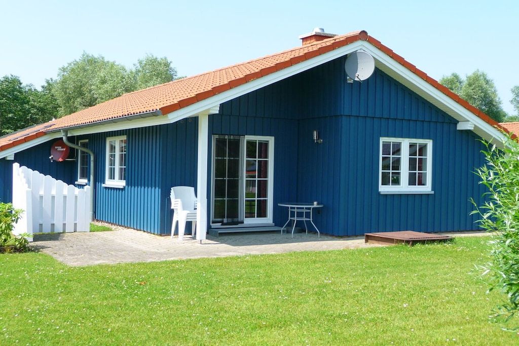 A blue building with a red roof, a white fence, and a small patio with a table and chairs.