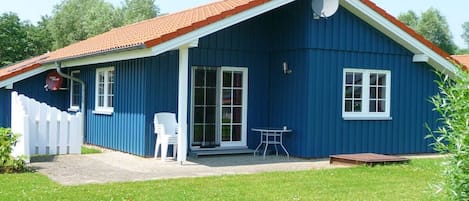 A blue building with a red roof, a white fence, and a small patio with a table and chairs.
