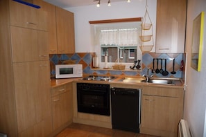 A compact kitchen with wooden cabinets, a microwave, stove, and dishwasher. - Holiday home with 1 bedroom (Otterndorf)