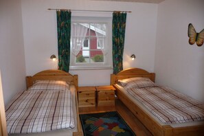 A bedroom with two wooden beds, a window with curtains, a butterfly wall decoration, and a small rug. - Holiday home with 1 bedroom (Otterndorf)