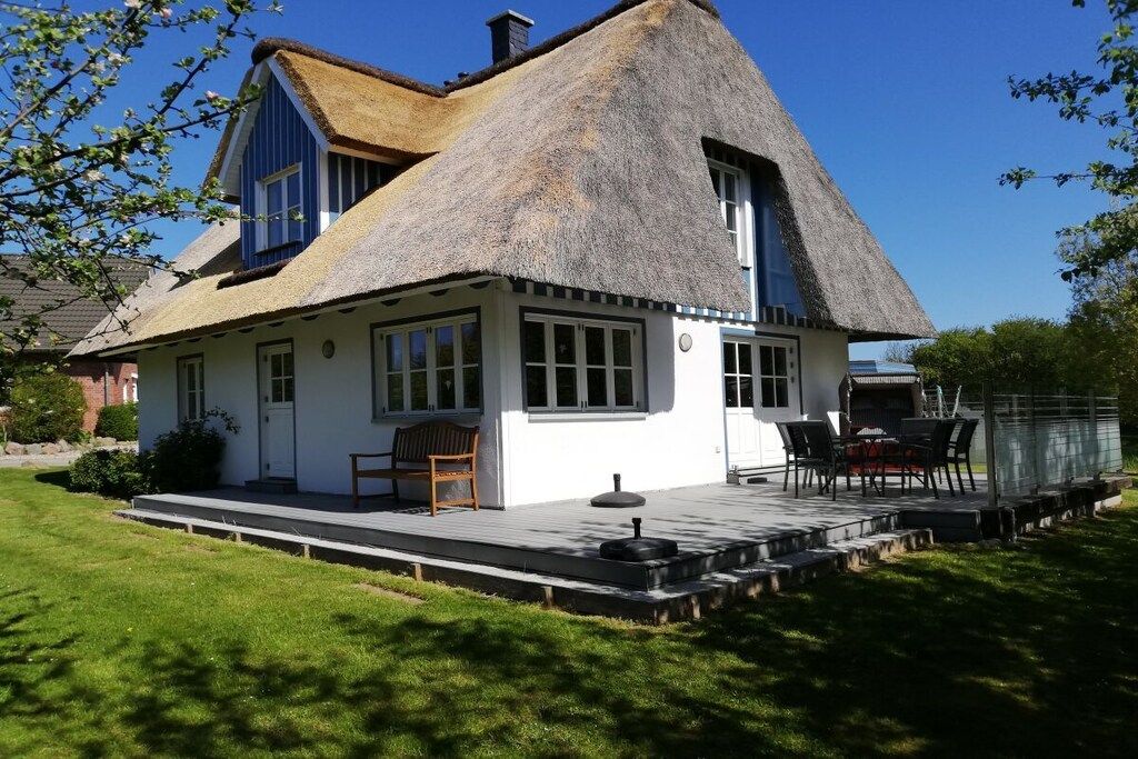 Ett hus med ett halmtak, en veranda med en bänk och en liten sittplats utomhus.