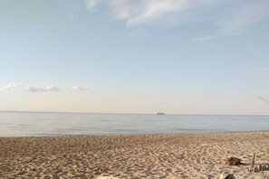 En strand med ett lugnt hav, ett avlägset fartyg och en klar himmel.