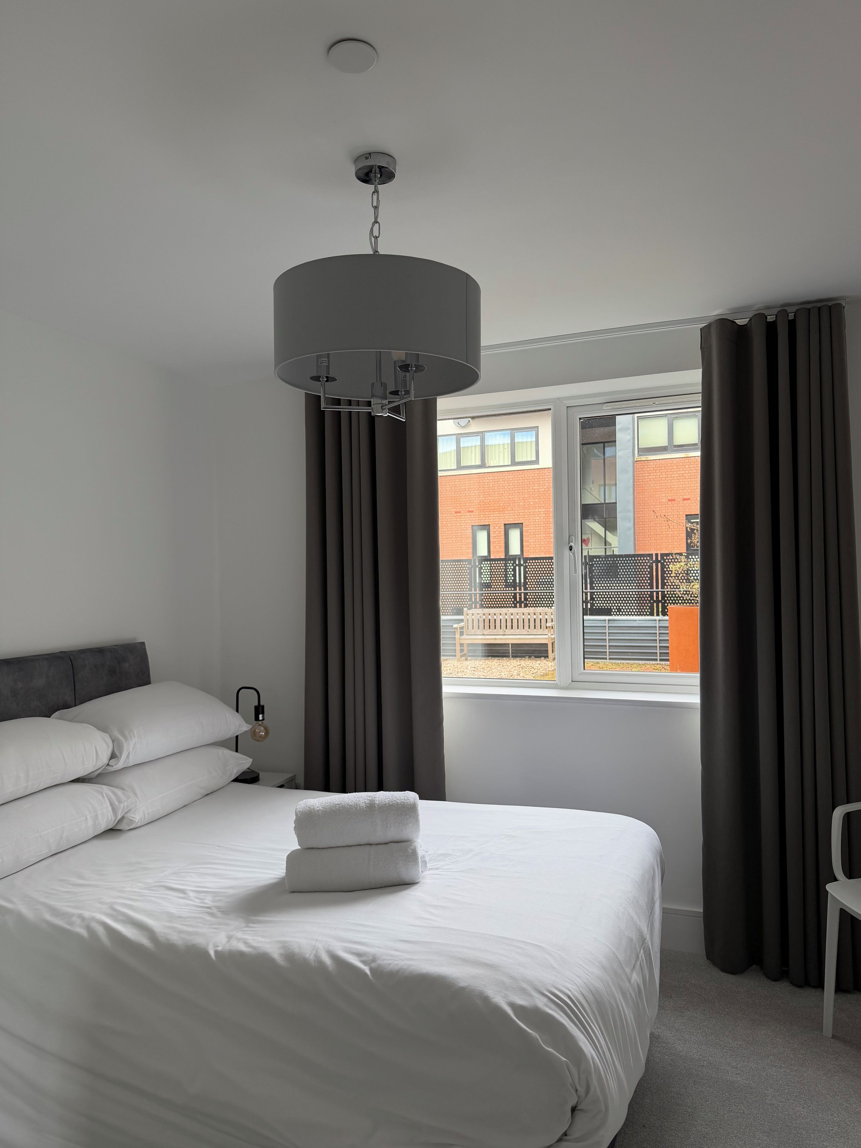 A hotel room with a bed, a window with curtains, a ceiling light fixture, and a view of the outside.