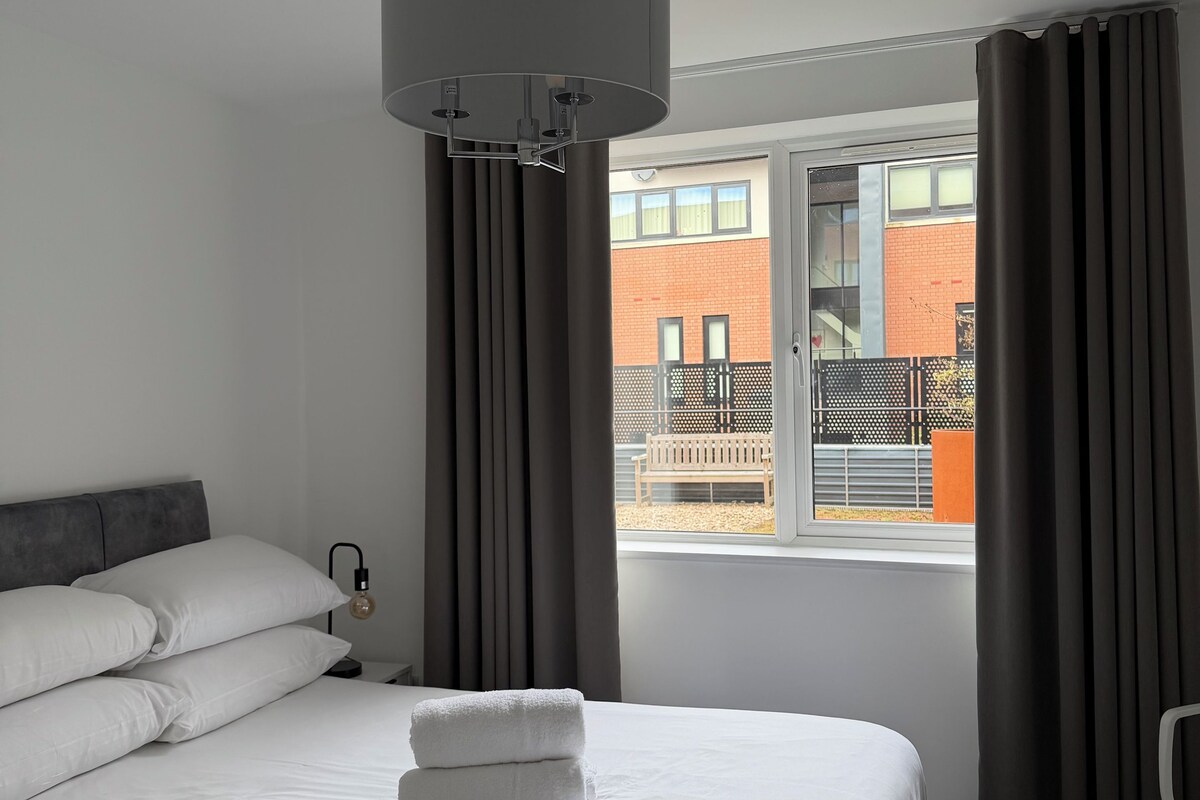 A hotel room with a bed, a window with curtains, a ceiling light fixture, and a view of the outside.