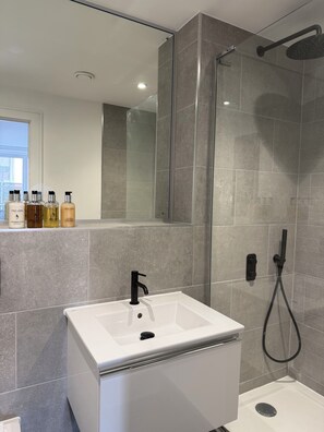 A modern bathroom with a glass-enclosed shower, a white sink, and a mirror above it. - The Lane Apartments by Urban Space (Cardiff)