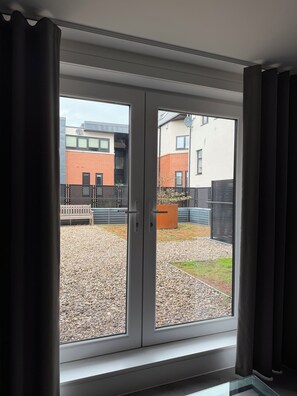 A room with a sliding glass door leading to an outdoor area with a gravel path, a wooden bench, and a metal fence. - The Lane Apartments by Urban Space (Cardiff)