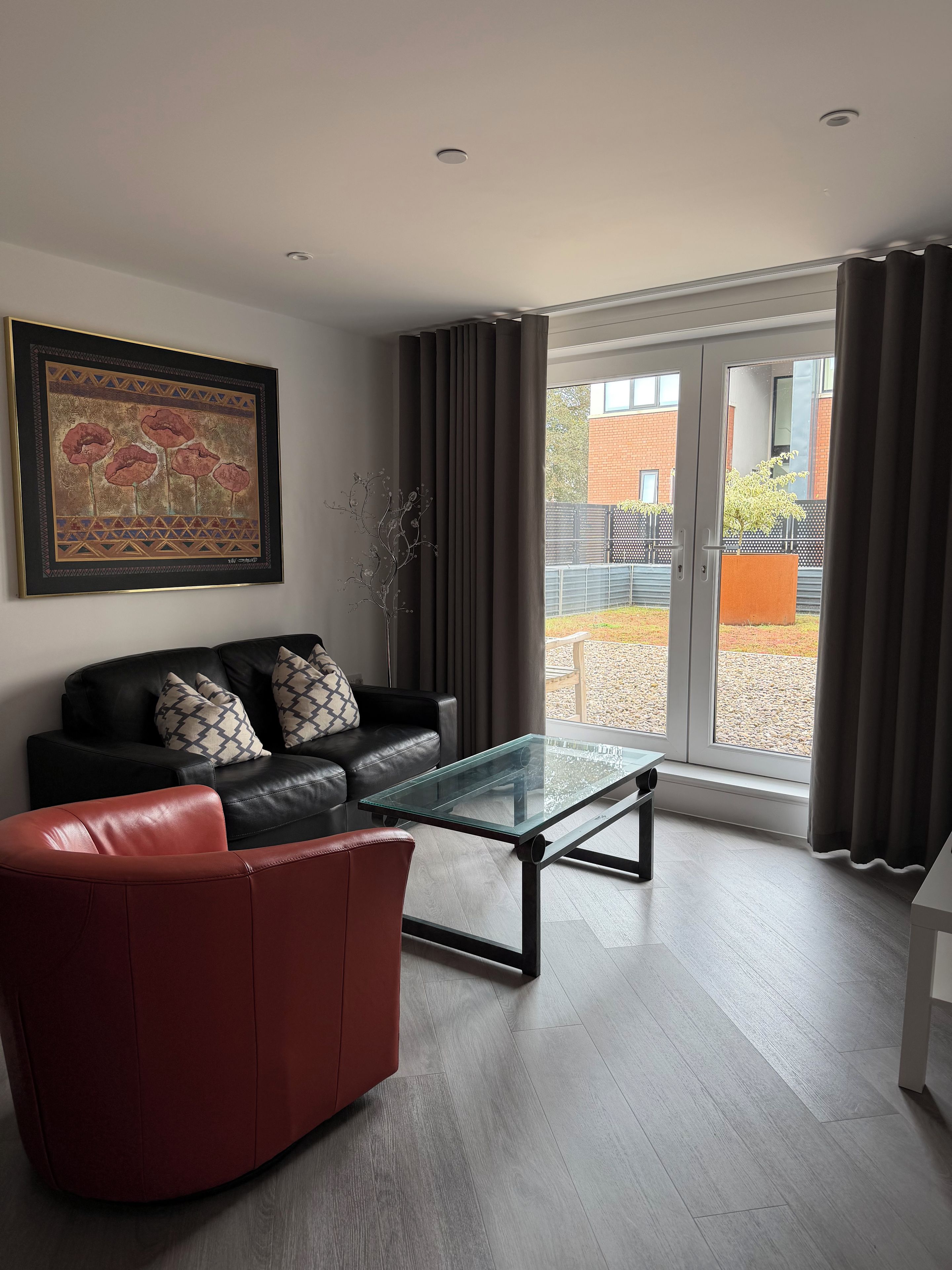 A modern living room with a glass coffee table, leather sofa, and a large framed artwork.