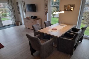 A dining area with a wooden table, six chairs, a television on the wall, and a view of the outdoors. - Holiday home with 4 bedrooms (Hooksiel Wangerland)