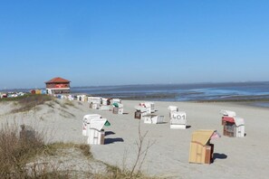 A beach with numbered beach huts and a red-roofed building in the background. - Holiday home with 4 bedrooms (Hooksiel Wangerland)