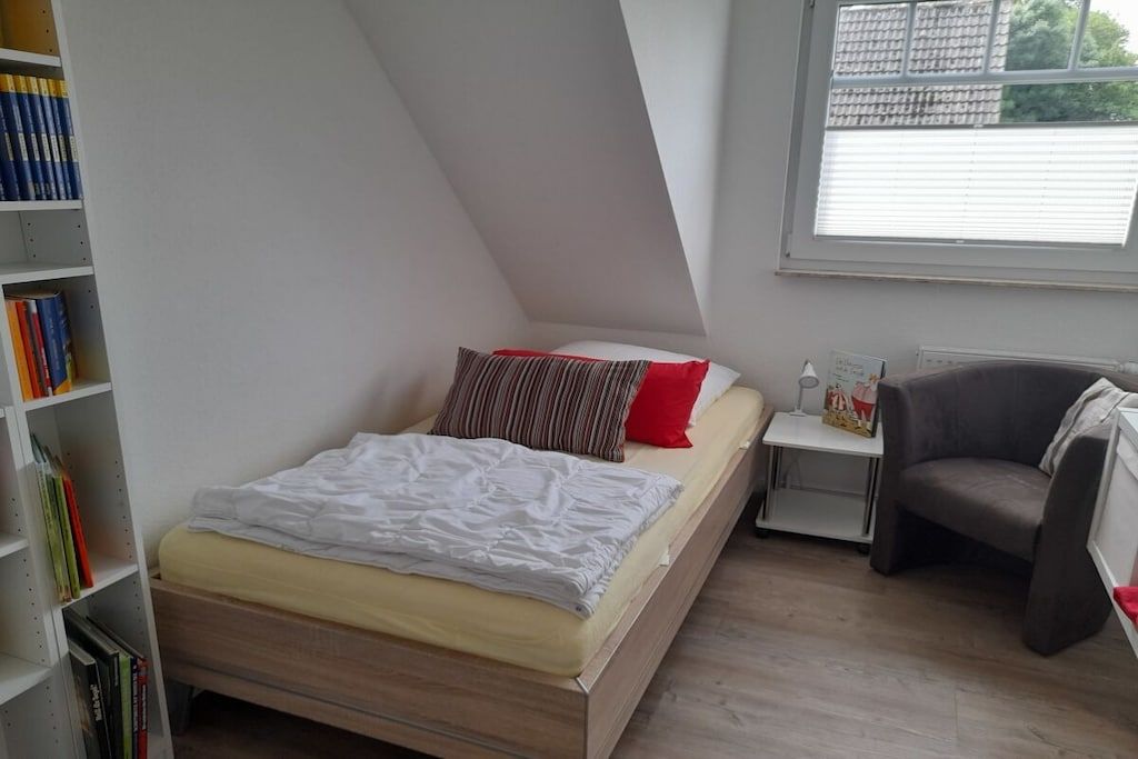 A bedroom with a bed, a nightstand, a chair, and a bookshelf.
