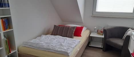 A bedroom with a bed, a nightstand, a chair, and a bookshelf.