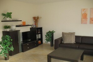 A modern living room with a dark brown sofa, a flat-screen TV, a coffee table, and decorative plants. - Holiday home with 3 bedrooms (Boltenhagen)